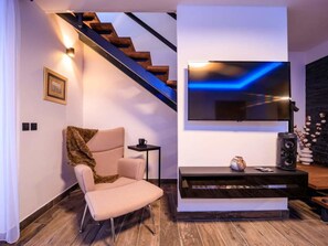 A modern living room with a sofa, a television mounted on the wall, and a staircase.