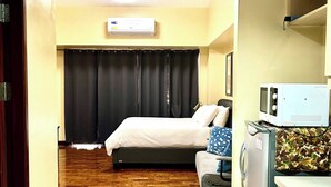 Habitación de hotel con cama, sofá, microondas, refrigerador y aire acondicionado.