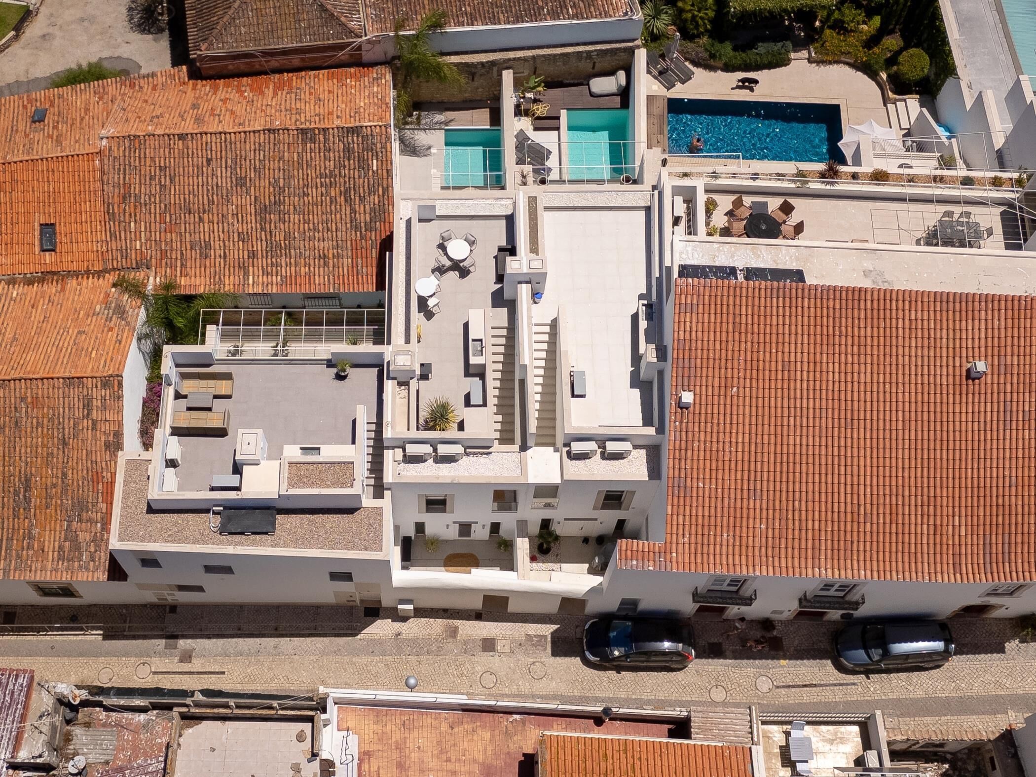 An aerial view of a building with a rooftop terrace, a swimming pool, and a parking area.