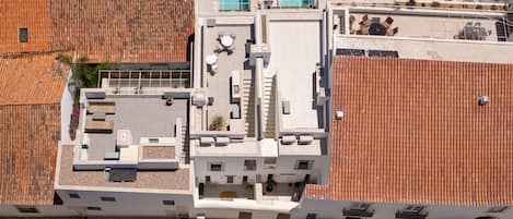 An aerial view of a building with a rooftop terrace, a swimming pool, and a parking area.