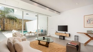 Una sala de estar moderna con una mesa de centro de vidrio, un sofá y un televisor sobre un mueble de madera.