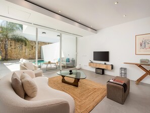 A modern living room with a glass coffee table, a sofa, and a television on a wooden stand. - Luxury Villa, Sea View and Pool, Central Lagos (Lagos)