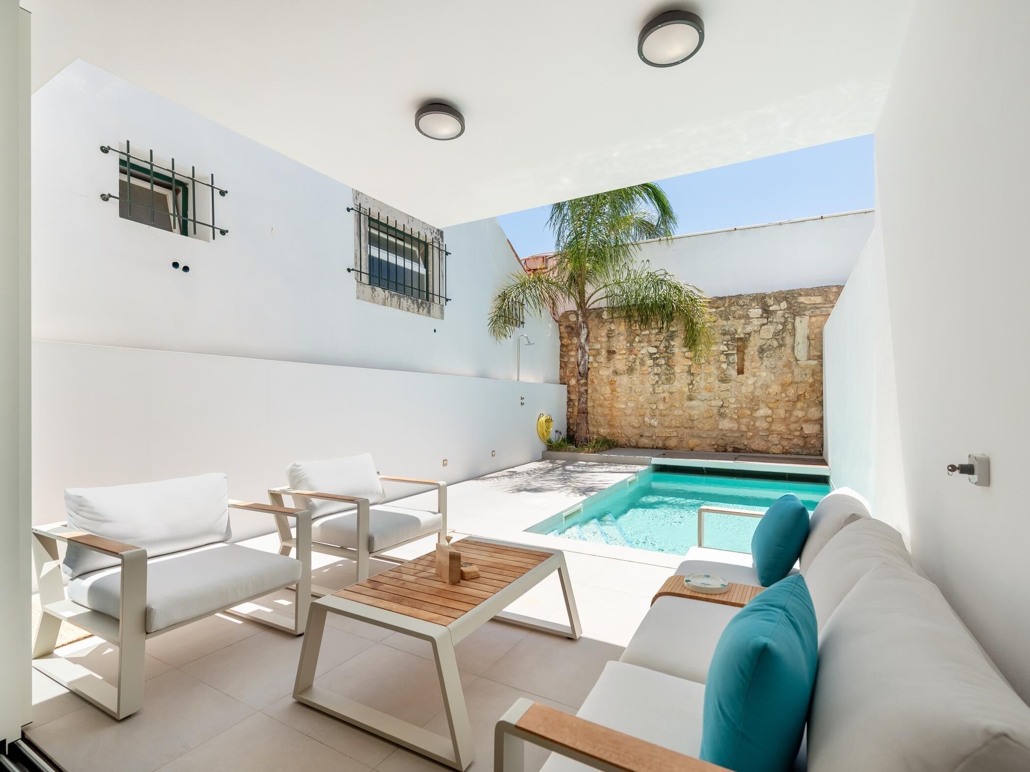 A modern outdoor living space with a pool, white furniture, and a stone wall.