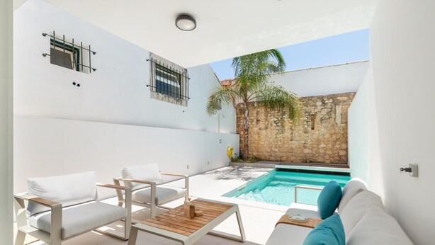 Un espacio exterior moderno con piscina, mobiliario blanco y una pared de piedra.