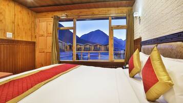 Habitación de hotel con una cama grande, paredes de madera, una ventana con vistas a la montaña y cabecero de madera.