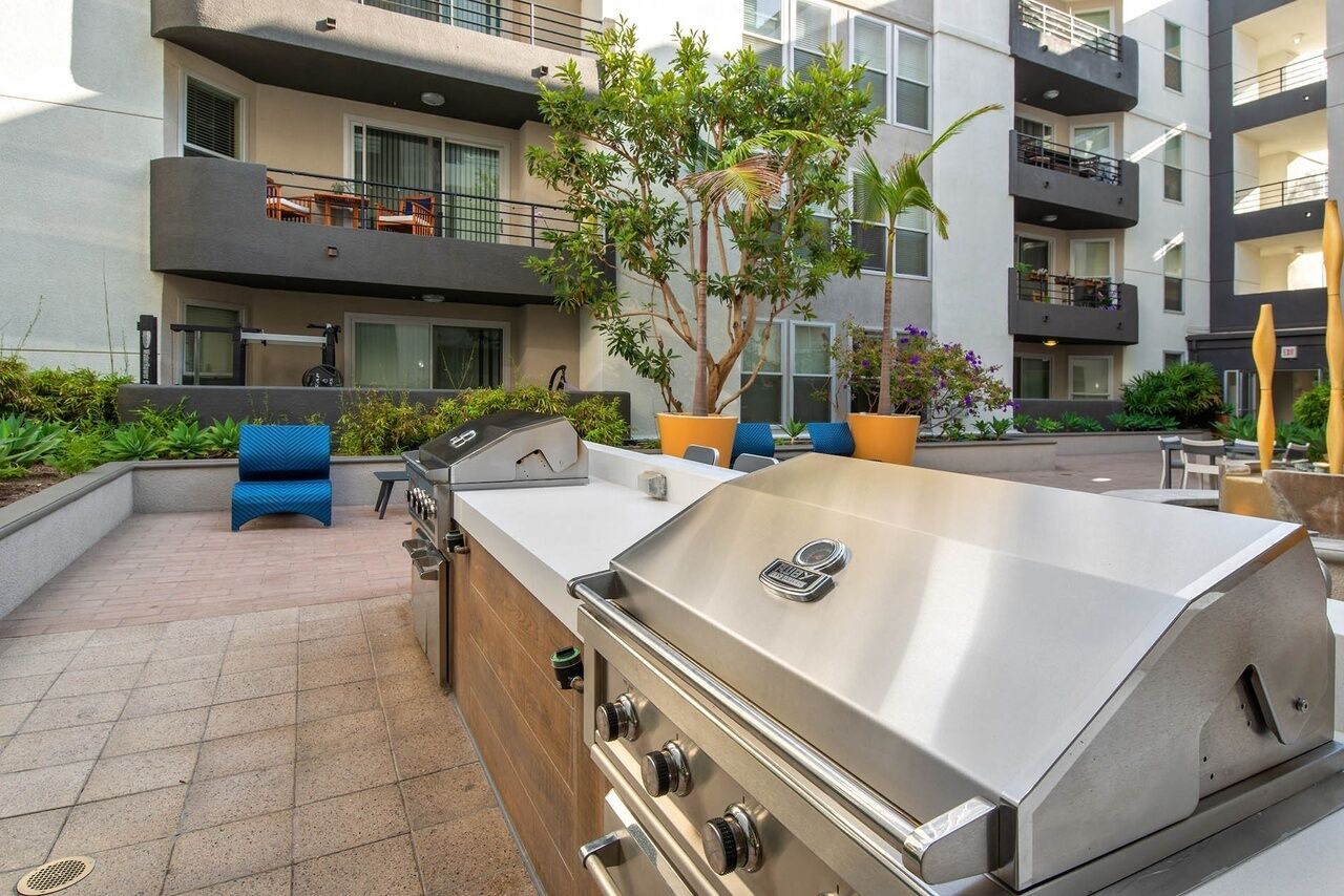 Une terrasse extérieure dotée d’un barbecue en acier inoxydable, de sièges bleus et de plantes en pot.