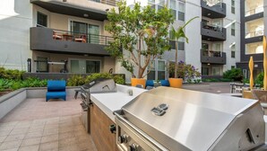 Un patio al aire libre con una parrilla de acero inoxidable, asientos azules y plantas en macetas.