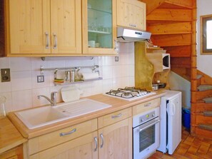 A compact kitchen with wooden cabinets, a gas stove, a microwave, and a small oven. - Vista Mont Blanc by Interhome (Celliers)