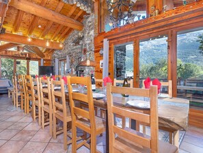 A wooden interior with a long dining table and chairs, stone walls, and a view of mountains through large windows. - Chalet Villaroger by Interhome (Villaroger)