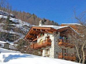 Un chalet à la façade en pierre, doté de balcons en bois et d’un toit recouvert de neige.