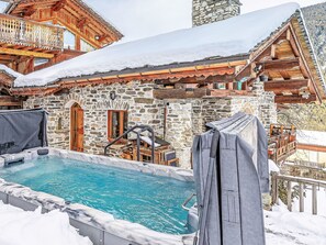 Un bâtiment en pierre doté d’une piscine, de balcons en bois et d’un espace extérieur aménagé avec des sièges, protégé par un toit.