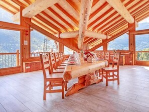 A wooden dining area with a long table set for a meal, surrounded by chairs, and large windows offering a view of the outdoors. - Perle des Neiges by Interhome (Villaroger)