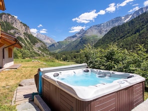 A hot tub in a mountainous area with a wooden deck and a house in the background. - Chalet Cairn by Interhome (Peisey-Nancroix)