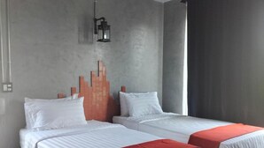 Une chambre d’hôtel avec deux lits, un mur décoratif en briques, un luminaire suspendu et une fenêtre avec des rideaux.