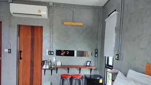Une chambre d’hôtel moderne équipée d’un lit, d’un bureau avec deux tabourets, d’une petite kitchenette et d’un appareil de climatisation.