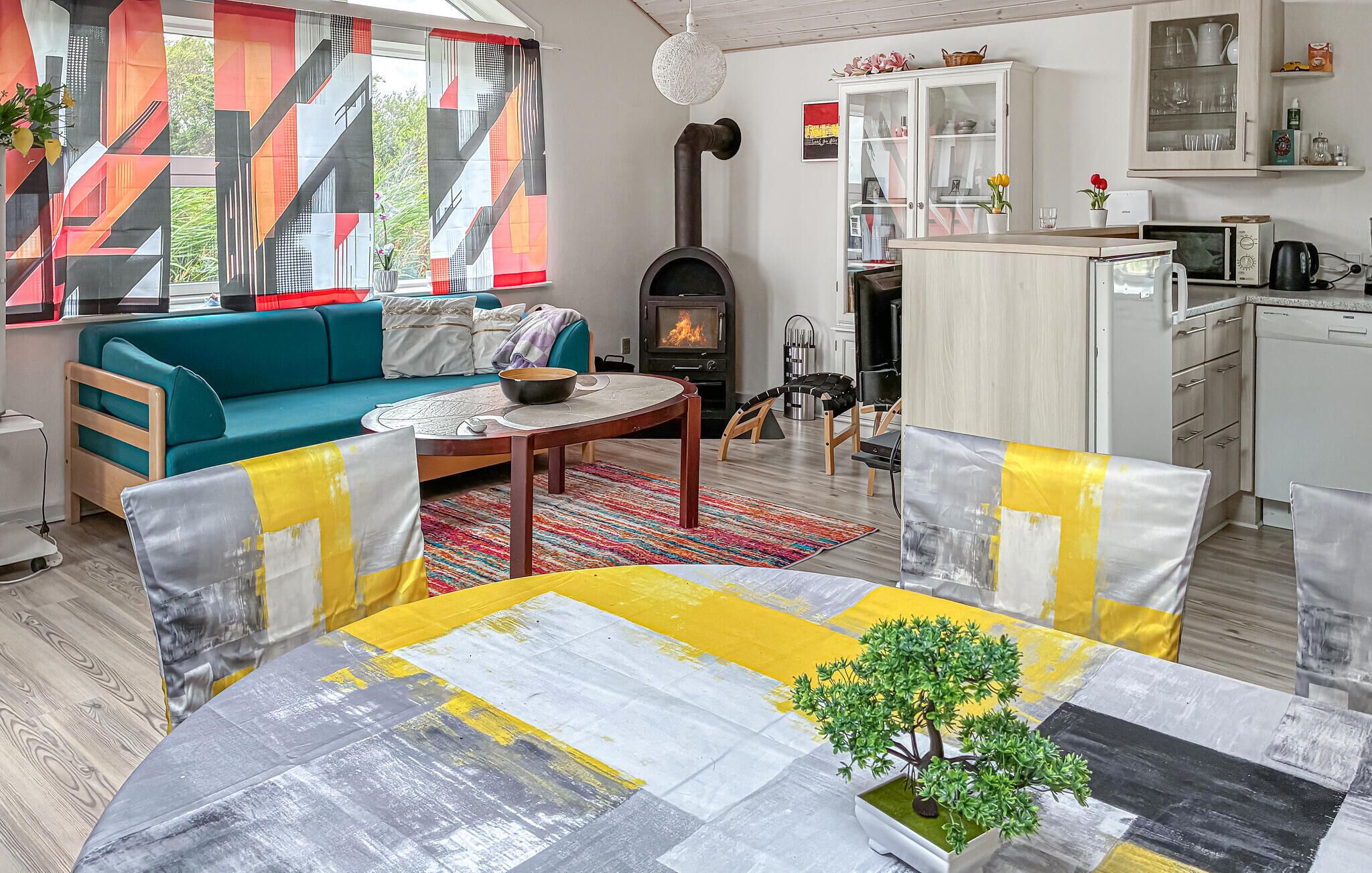 A living room with a sofa, coffee table, and a fireplace. There is a kitchen area with cabinets and a microwave.