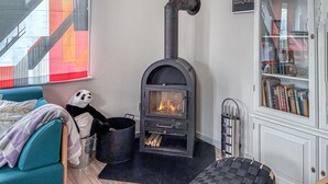 Una habitación acogedora con un estufa de leña negra, un sofá, un peluche de panda y una estantería.