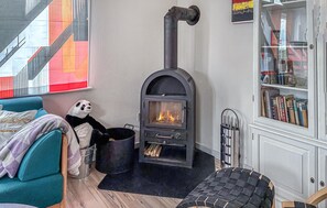 Ein gemütliches Zimmer mit einem schwarzen Kaminofen, einer Couch, einem Panda-Plüschtier und einem Bücherregal.