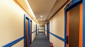 A hotel corridor with doors on both sides, a fire extinguisher on the floor, and a number '216' on the wall.
