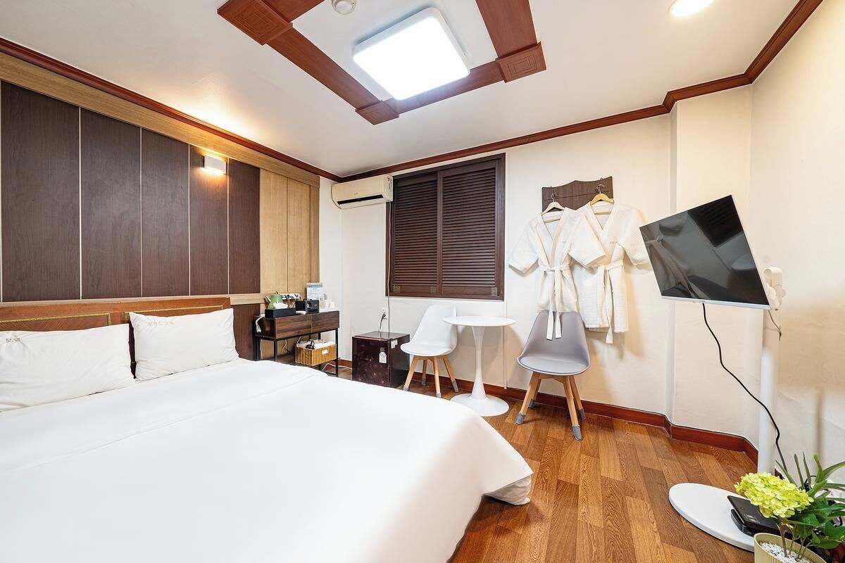 Una habitación de hotel con una cama grande, un escritorio, dos sillas, un televisor y una ventana con persianas.