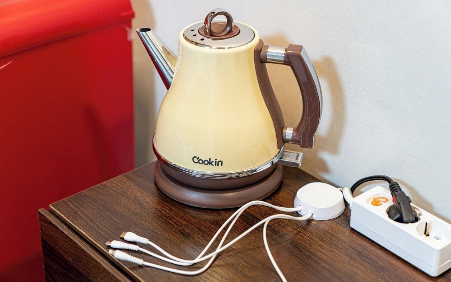 A Cookin electric kettle on a wooden table with a power cord and a power adapter.