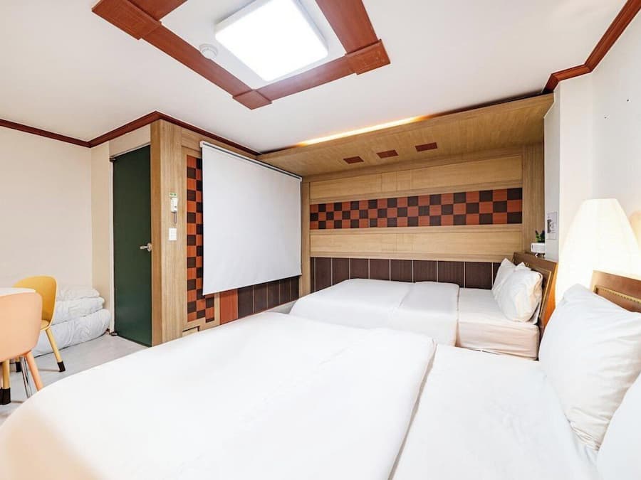 Une chambre d’hôtel avec deux lits, un bureau, une chaise, un mur à carreaux et une lucarne.