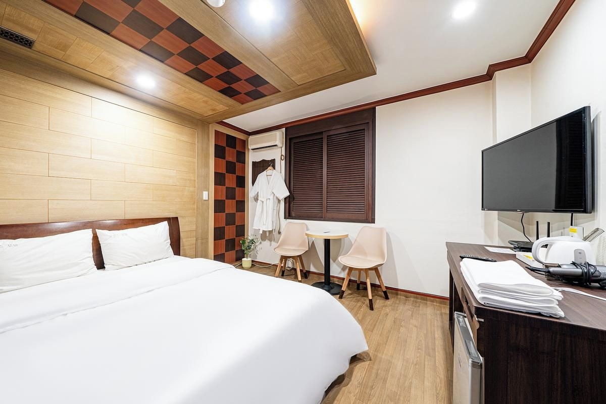 Habitación de hotel con cama, escritorio con televisor, una silla y una mesita.