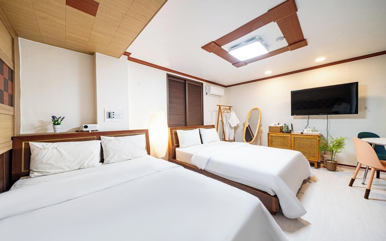 A hotel room with two beds, a television, a desk with a chair, and a ceiling fan.