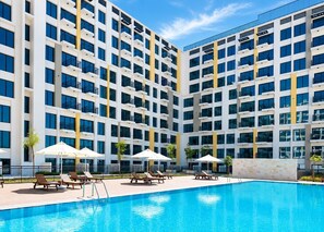 A modern hotel with a swimming pool, multiple balconies, and sun loungers. - UNA Apartments - Town Square Dubai (Dubai)