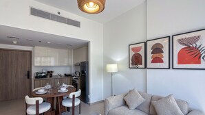 Una sala de estar moderna con sofá, mesa de comedor y sillas. Hay una zona de cocina con armarios y electrodomésticos.