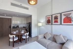 A modern living room with a sofa, dining table, and chairs. There is a kitchen area with cabinets and appliances. - UNA Apartments - Town Square Dubai (Dubai)