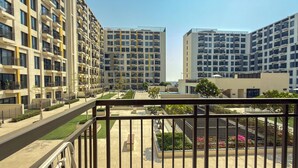 Un edificio residencial moderno con varios balcones, un jardín cuidado y un cielo despejado.