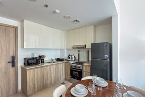 A modern kitchen with a built-in microwave, toaster, and stove, a refrigerator, and a dining area with a table set for two. - UNA Apartments - Town Square Dubai (Dubai)