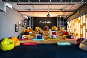 Ein Kino mit dunklem Boden, bunten Sitzplätzen und einem Projektor an der Decke.