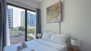 Una habitación de hotel con una cama, dos lámparas de noche, un ventanal con cortinas y una obra de arte colgada en la pared.