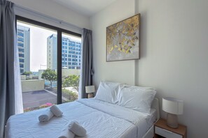 A hotel room with a bed, two bedside lamps, a window with curtains, and a wall-mounted artwork. - UNA Apartments - Town Square Dubai (Dubai)