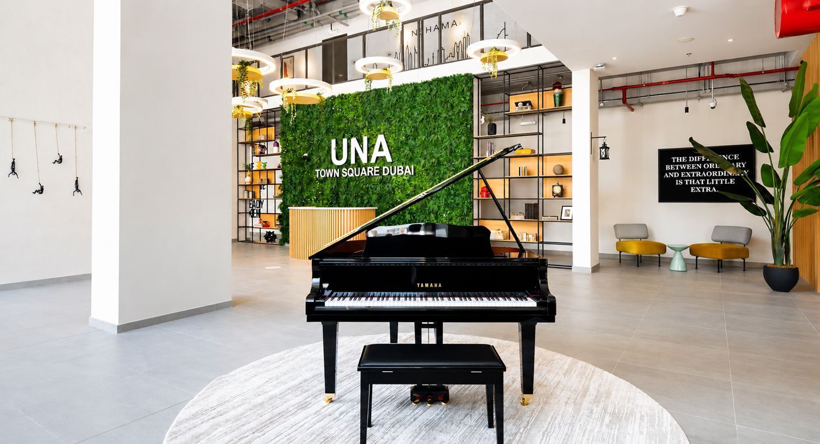 A grand piano in a modern lobby with a green wall and a sign reading 'UNA TOWN SQUARE DUBAI'.
