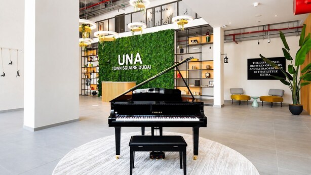 Un piano de cola en un moderno vestíbulo con una pared verde y un cartel que dice 'UNA TOWN SQUARE DUBAI'.