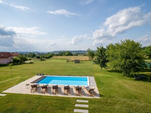 Ein rechteckiger Swimmingpool mit glasklar blauem Wasser, umgeben von einer gepflasterten Liegefläche mit sechs Liegestühlen und einem kleinen Tisch.