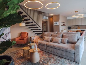 Ein modernes Wohnzimmer mit Sofa, Sessel, Treppe und Küchenzeile.