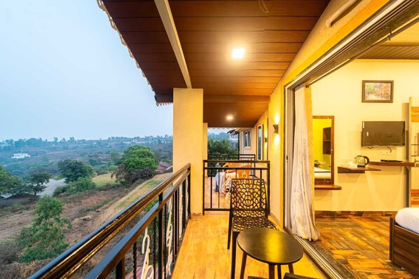 A balcony with a view of a rural landscape, a bed, a TV, and a table.