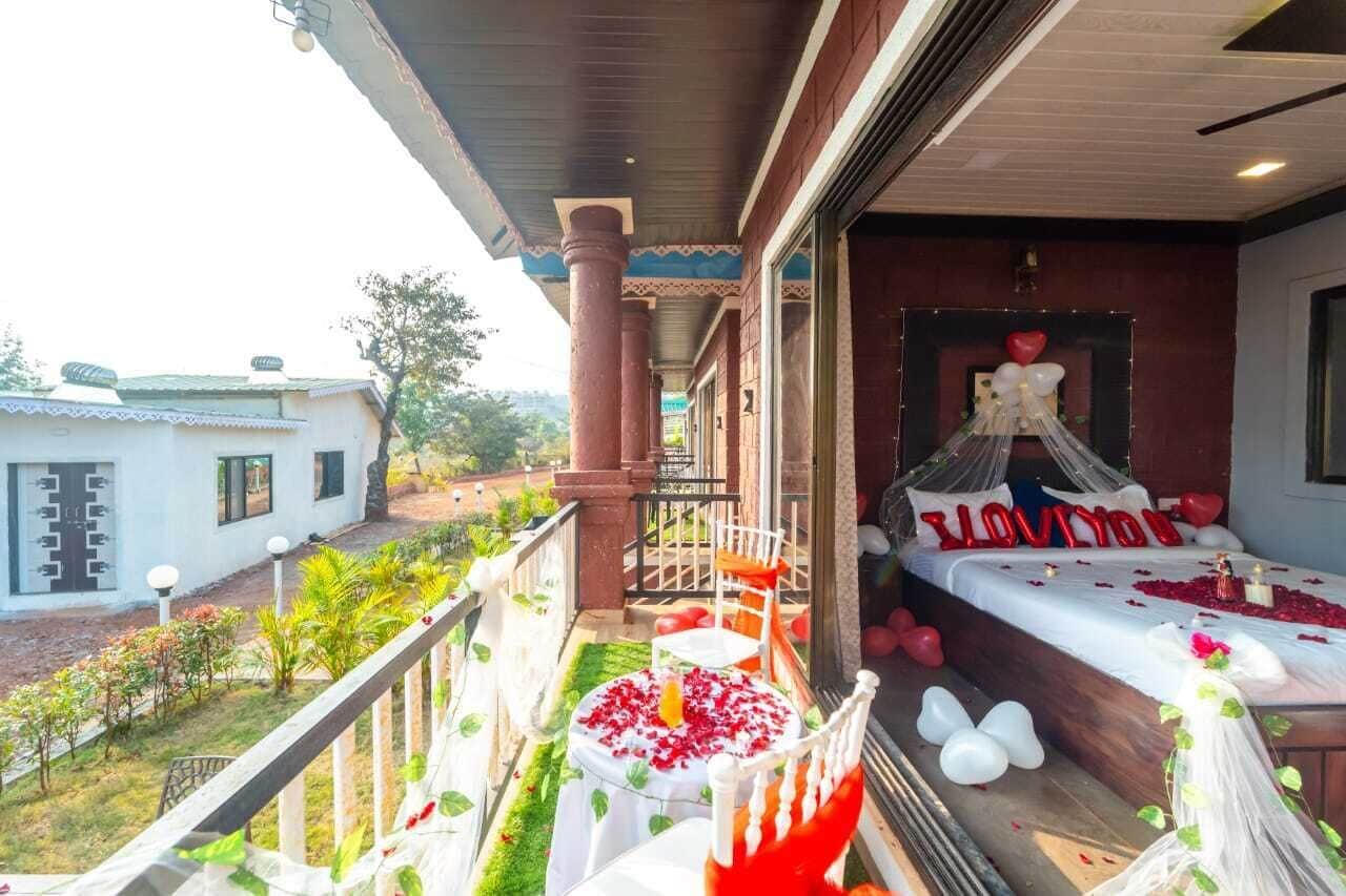 A balcony with a view of a garden and a room with a bed decorated with balloons and a heart-shaped pillow.