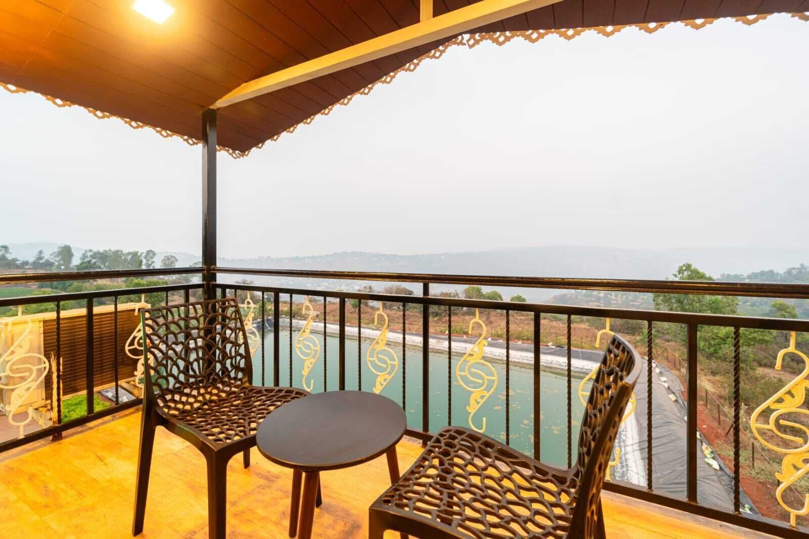 A balcony with two chairs and a small table, overlooking a river and distant landscape.