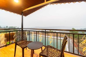 A balcony with two chairs and a small table, overlooking a river and distant landscape. - Hiltan Valley Resort (Mahabaleshwar)