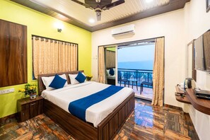 Quarto de hotel com cama, mesa de cabeceira, escrivaninha e varanda com vista.
