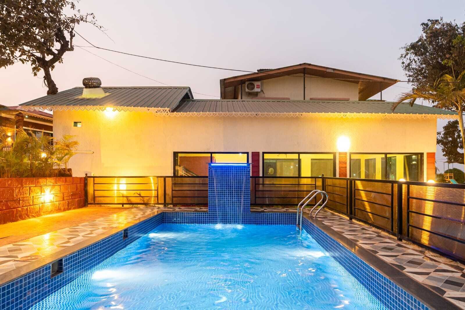 Una piscina con un borde de baldosas, una escalera de metal y un edificio con entrada de azulejos.