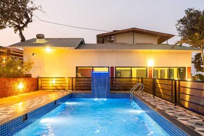 Una piscina con un borde de baldosas, una escalera de metal y un edificio con entrada de azulejos.