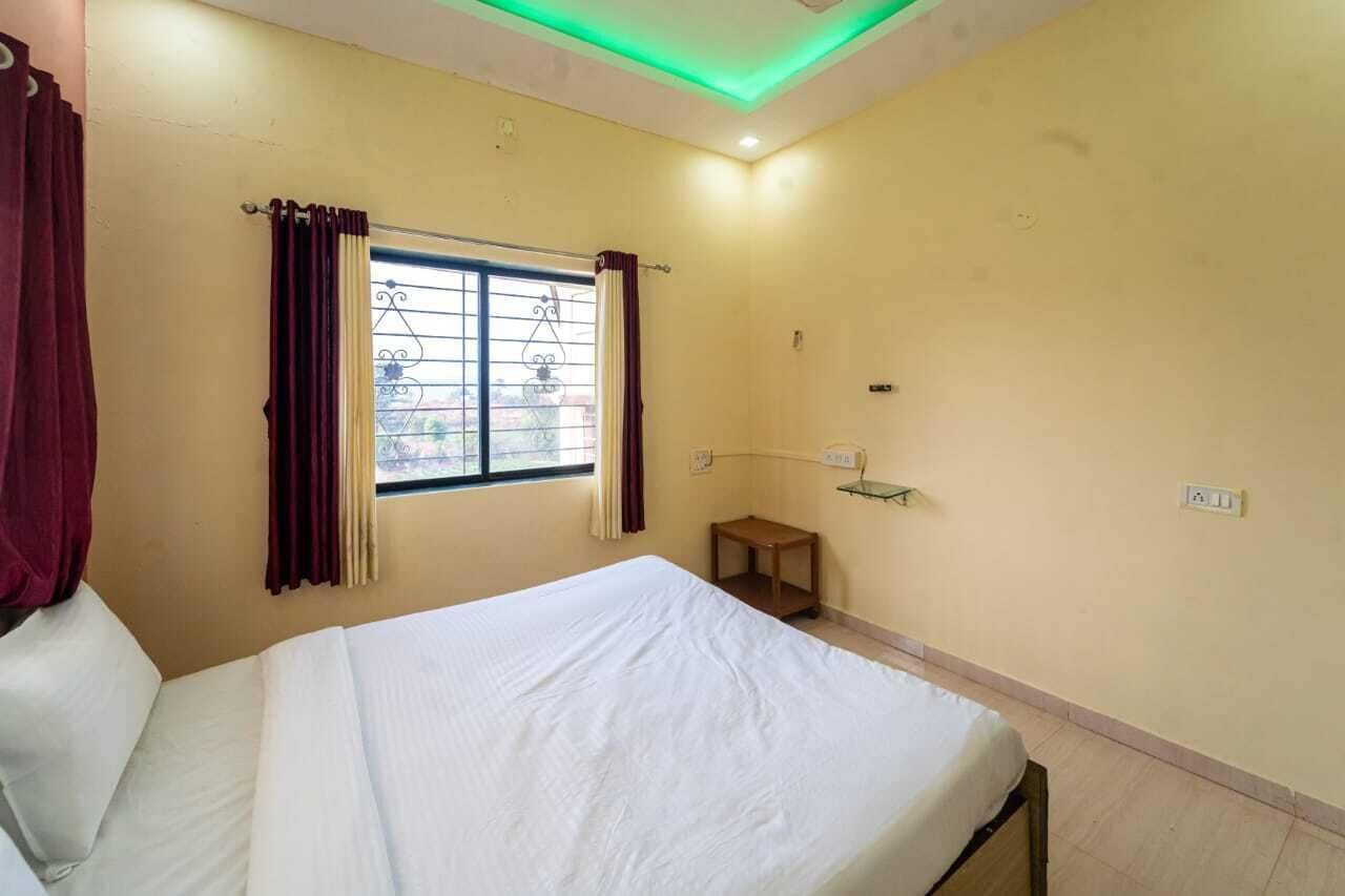 Habitación de hotel con cama, ventana con cortinas, una mesita y una estantería en la pared.