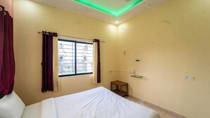 Ein Hotelzimmer mit Bett, einem Fenster mit Vorhängen, einem kleinen Tisch und einem an der Wand befestigten Regal.