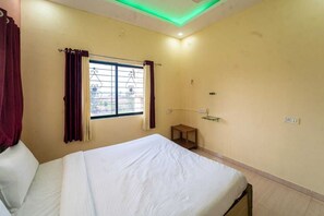 Habitación de hotel con cama, ventana con cortinas, una mesita y una estantería en la pared.